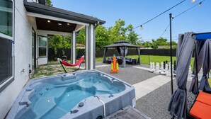 A modern outdoor hot tub area with a covered seating area and a gazebo.