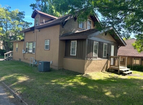 A two-story house with a front porch, a small deck, and a visible air conditioning unit.