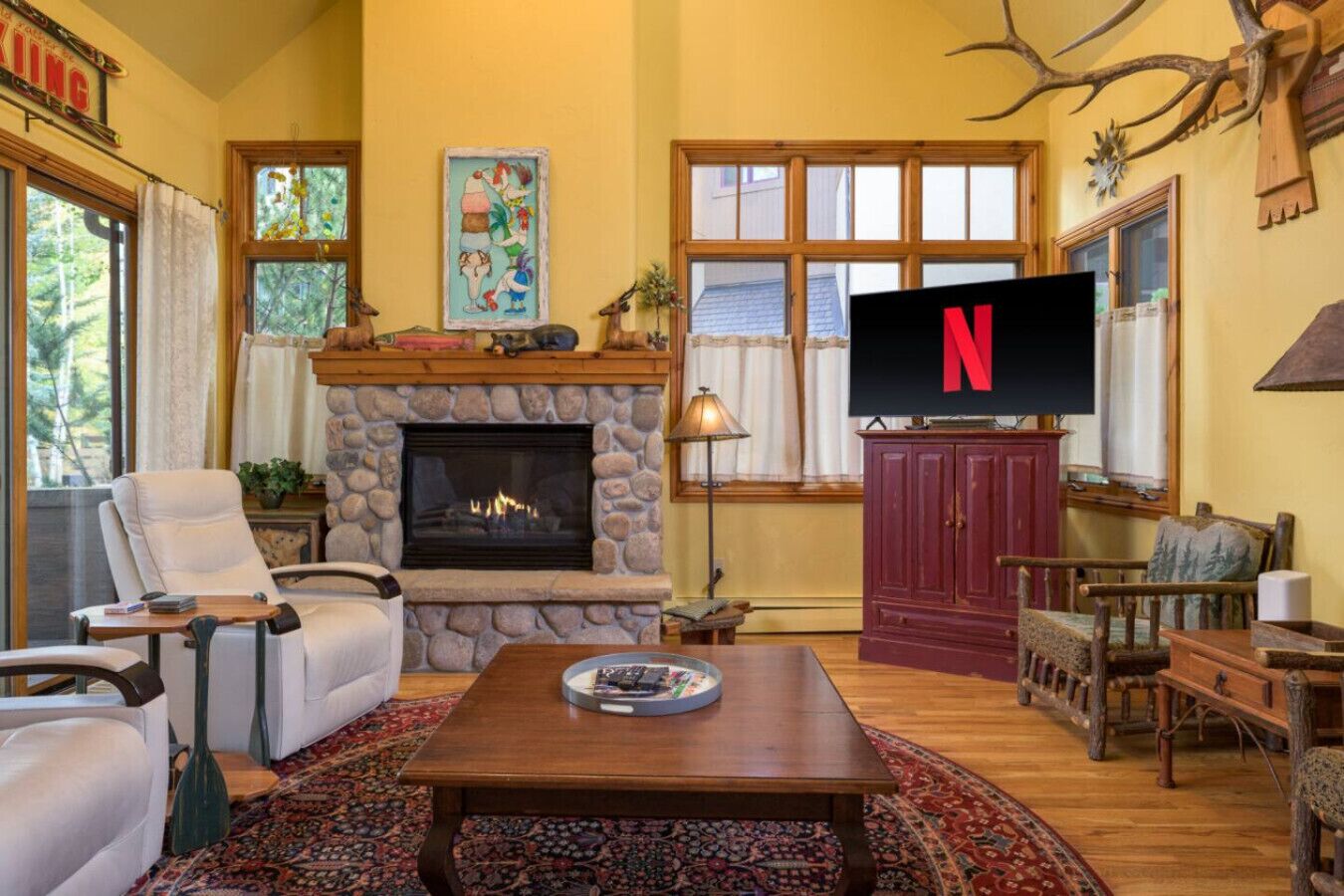 A cozy living room with a stone fireplace, comfortable seating, a television, and a large window.
