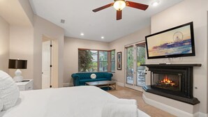 A bedroom with a bed, a blue sofa, a fireplace, a TV, and a ceiling fan. - The Huntington Spacious Family Friendly (Poway)