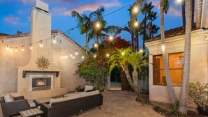 An outdoor patio with a fireplace, wicker furniture, and string lights. - The Huntington Spacious Family Friendly (Poway)