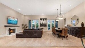 A spacious living room with a fireplace, a large sofa, a dining area with chairs, and a kitchen area with cabinets and a mirror. - The Huntington Spacious Family Friendly (Poway)