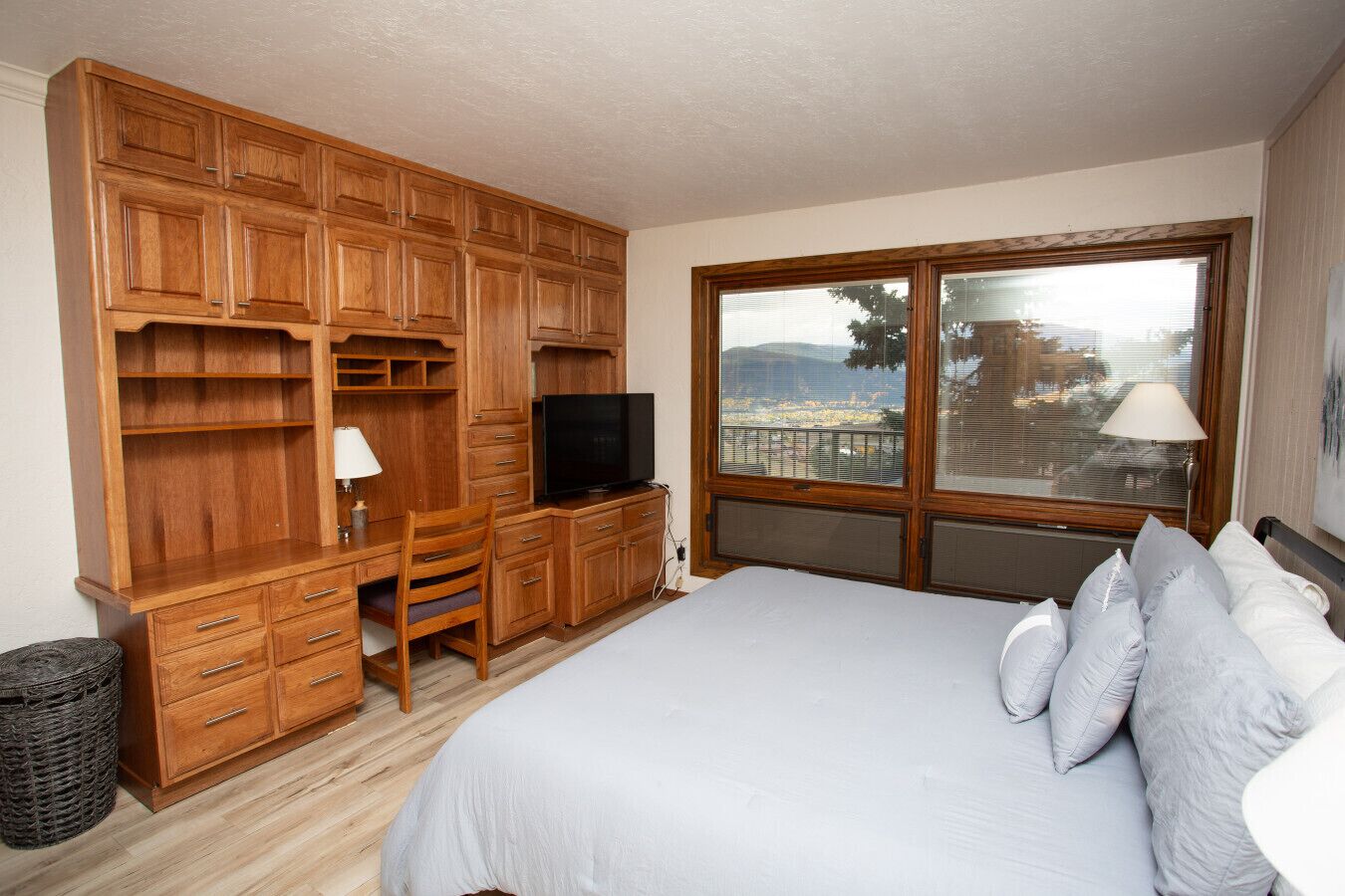Une chambre avec un grand lit, une armoire en bois, un bureau avec une chaise, une télévision et une fenêtre donnant sur la ville.