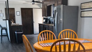 A dining area with a wooden table and chairs, a kitchen in the background, and a ceiling fan. - NEW GAME ROOM Quiet, Comfortable, Spacious Home Near OSU! (Stillwater)