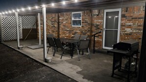 An outdoor patio with a brick wall, a table with chairs, a grill, and string lights. - NEW GAME ROOM Quiet, Comfortable, Spacious Home Near OSU! (Stillwater)