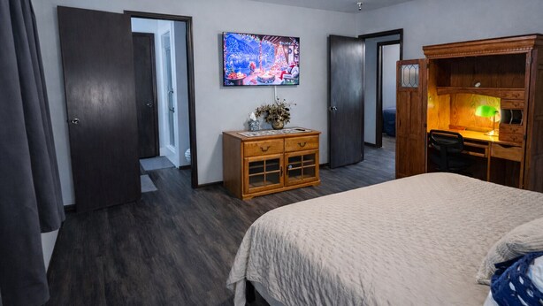 A hotel room with a large bed, a wooden dresser, a desk with a lamp, and a TV on the wall. - NEW GAME ROOM Quiet, Comfortable, Spacious Home Near OSU! (Stillwater)