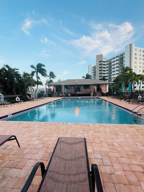 A swimming pool with lounge chairs, palm trees, and a building in the background.