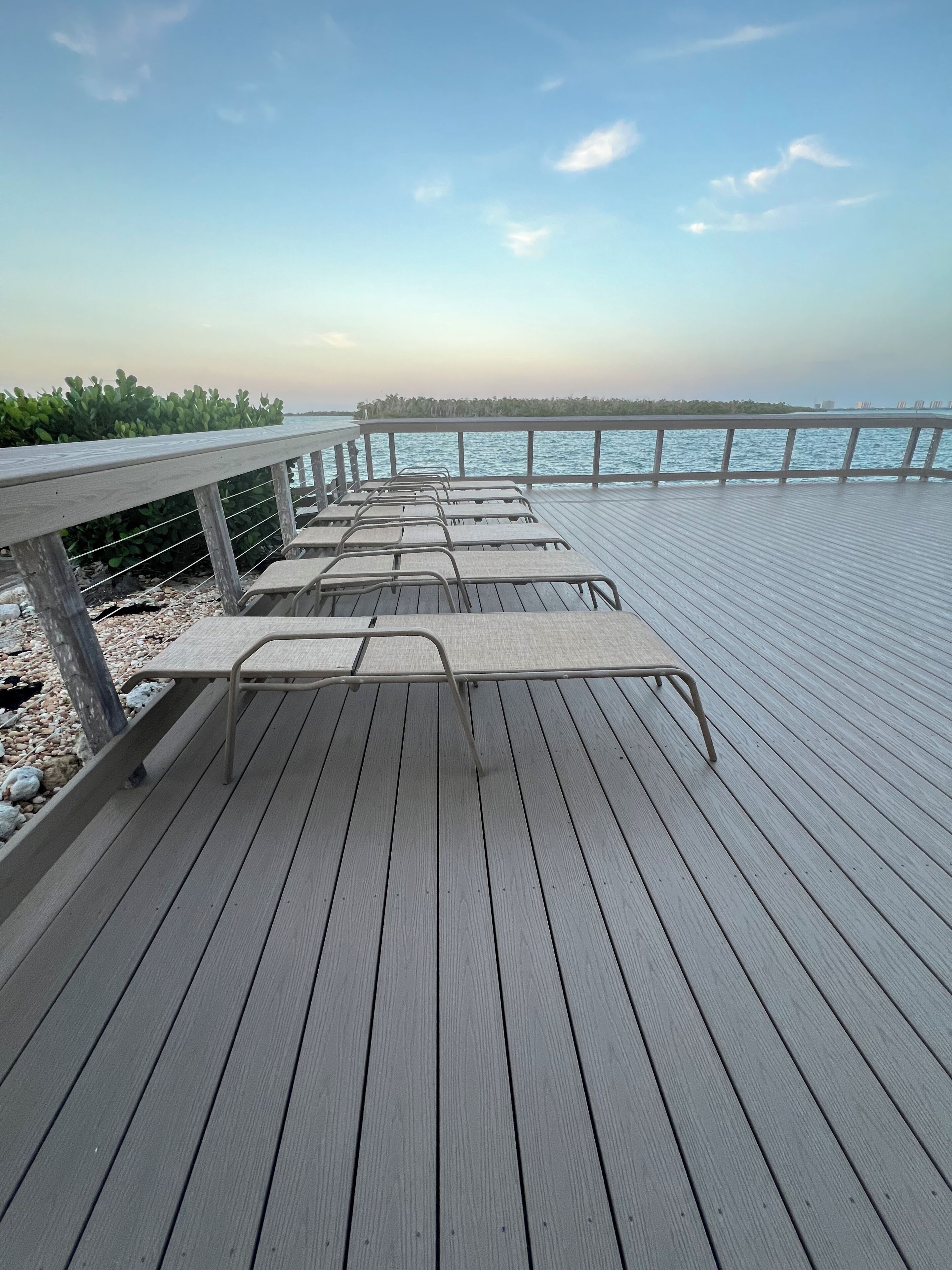 A wooden deck with metal chairs, a railing, and a view of the water.