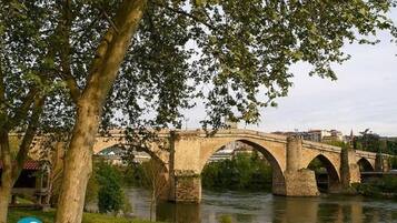 A stone bridge with multiple arches over a river, surrounded by trees and buildings in the background.