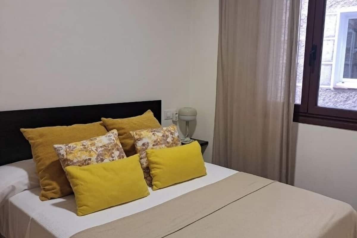 A bed with a black headboard, a beige bedspread, and multiple pillows in yellow and floral patterns.