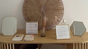 Une console en bois surmontée d’un objet circulaire tissé, de deux documents encadrés, d’un miroir hexagonal et d’un panier tressé.