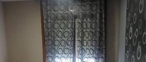 Quarto de hotel com duas camas, um radiador, cortinas estampadas e uma parede com desenhos circulares.