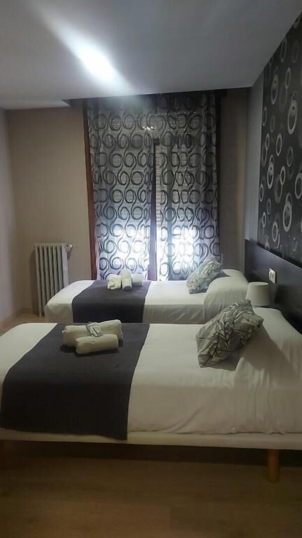A hotel room with two beds, a radiator, patterned curtains, and a wall with circular designs. - NEW JJ HOSTEL (Ourense)
