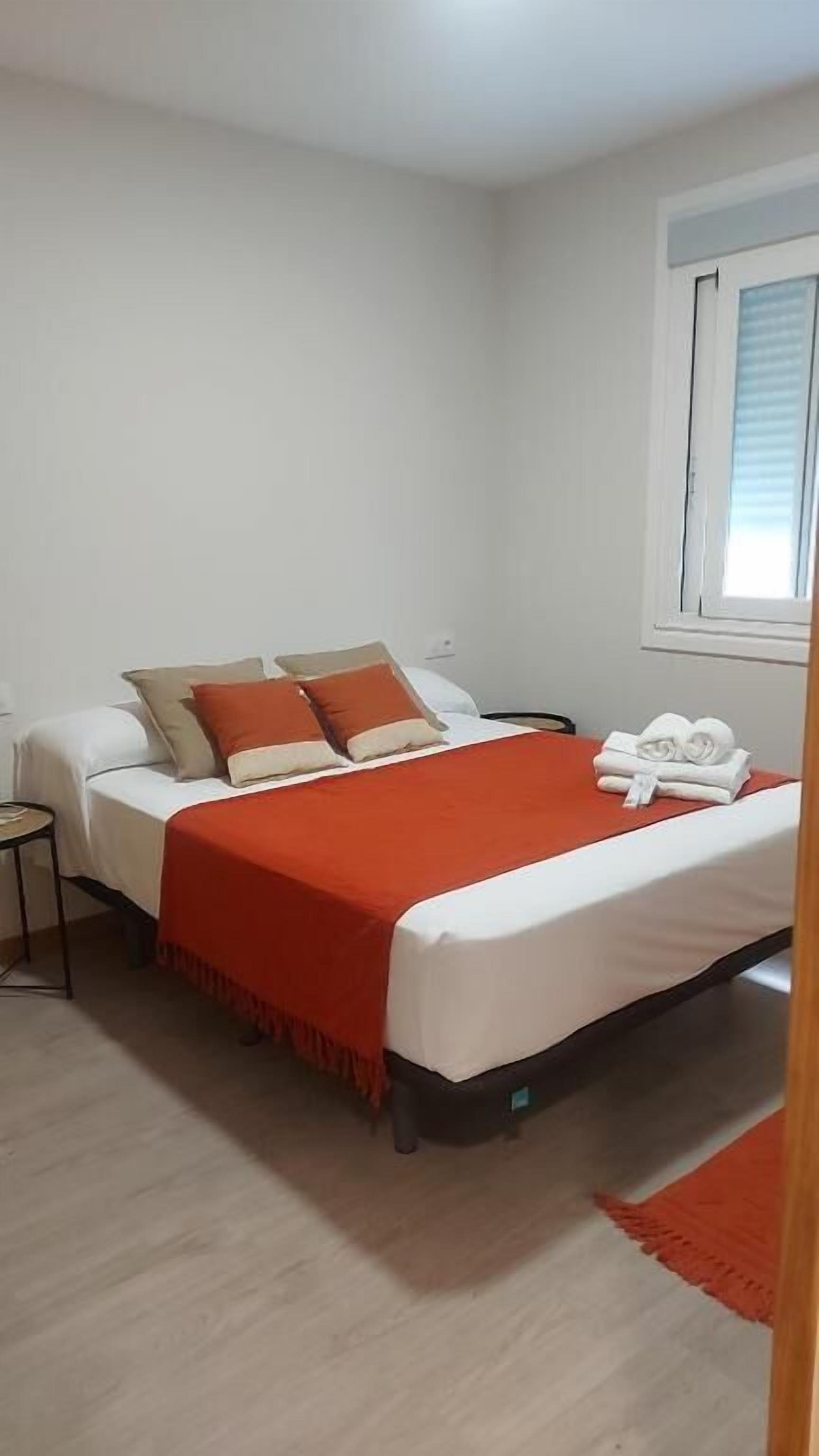Ein Schlafzimmer mit Bett, Kissen, einem Nachttisch, einem Fenster und einem roten Teppich.
