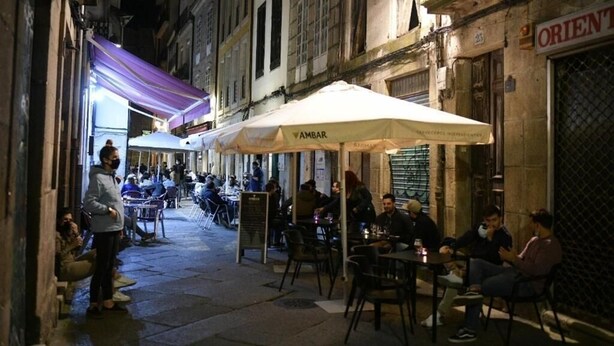 Un espace de café en plein air avec des tables, des chaises, des parasols, et des personnes assises ou debout.