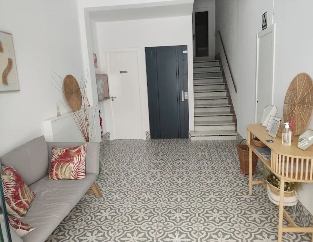 Ein modernes Interieur mit einem gemusterten Boden, einem grauen Sofa mit dekorativen Kissen, einem Holztisch mit einem Korb und einer Treppe, die in einen anderen Raum führt.