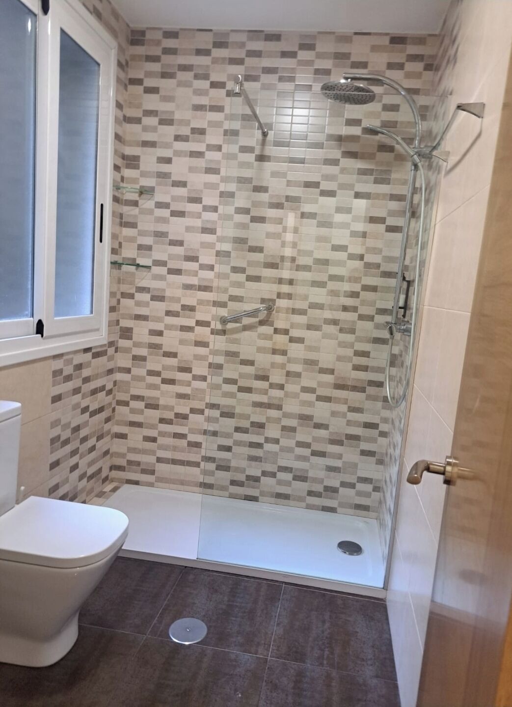 A small bathroom with a toilet, a shower with a glass door, and tiled walls.