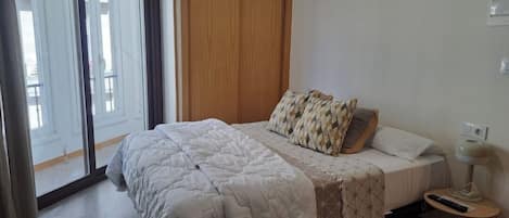 Un dormitorio con una cama, una mesita de noche, una lámpara y vistas a través de una ventana.
