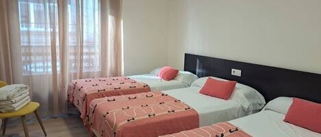 Habitación de hotel con tres camas, cada una con una colcha estampada en rosa y beige, y una silla con toallas dobladas.