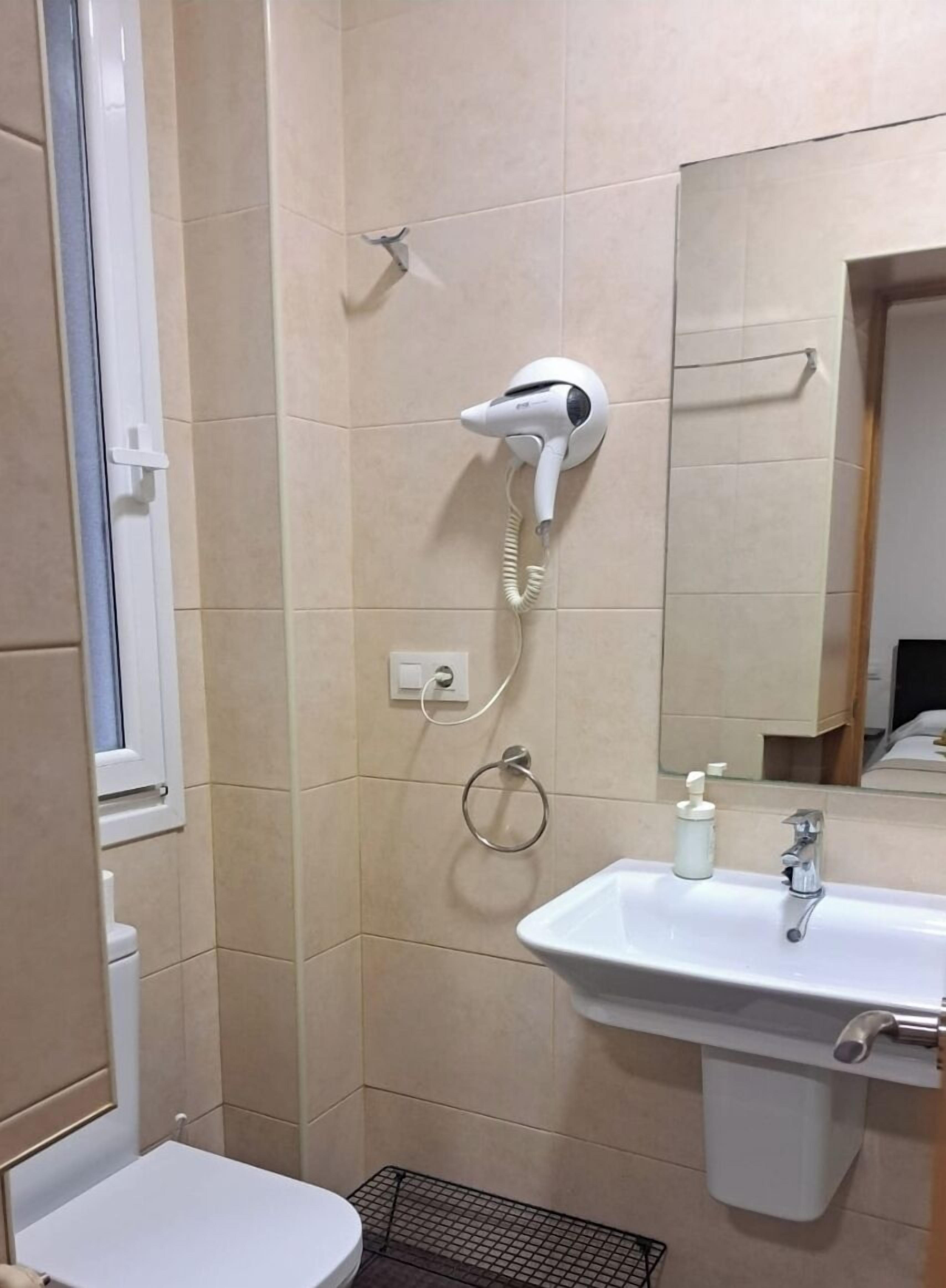 A bathroom with a white toilet, a sink with a mirror, and a hairdryer mounted on the wall.