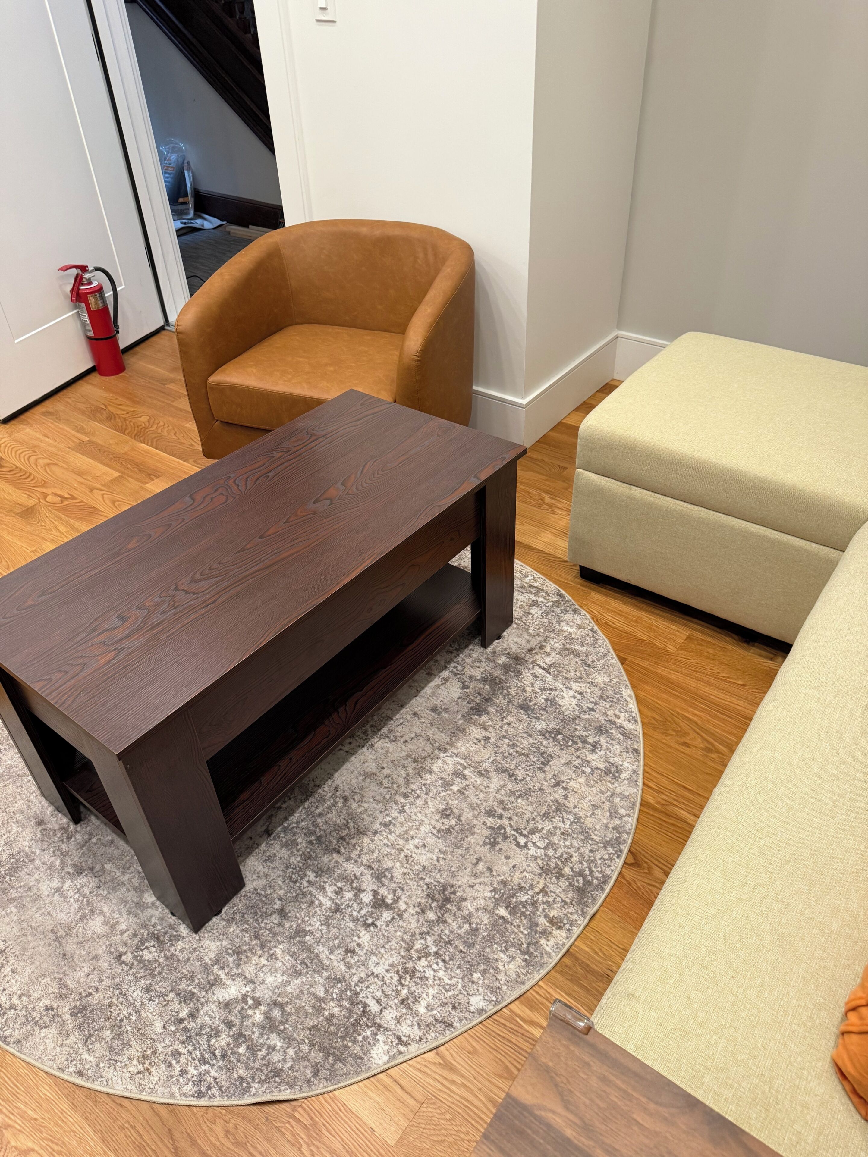Una habitación con una mesa de madera oscura, un sillón marrón, un sofá beige y una alfombra gris.