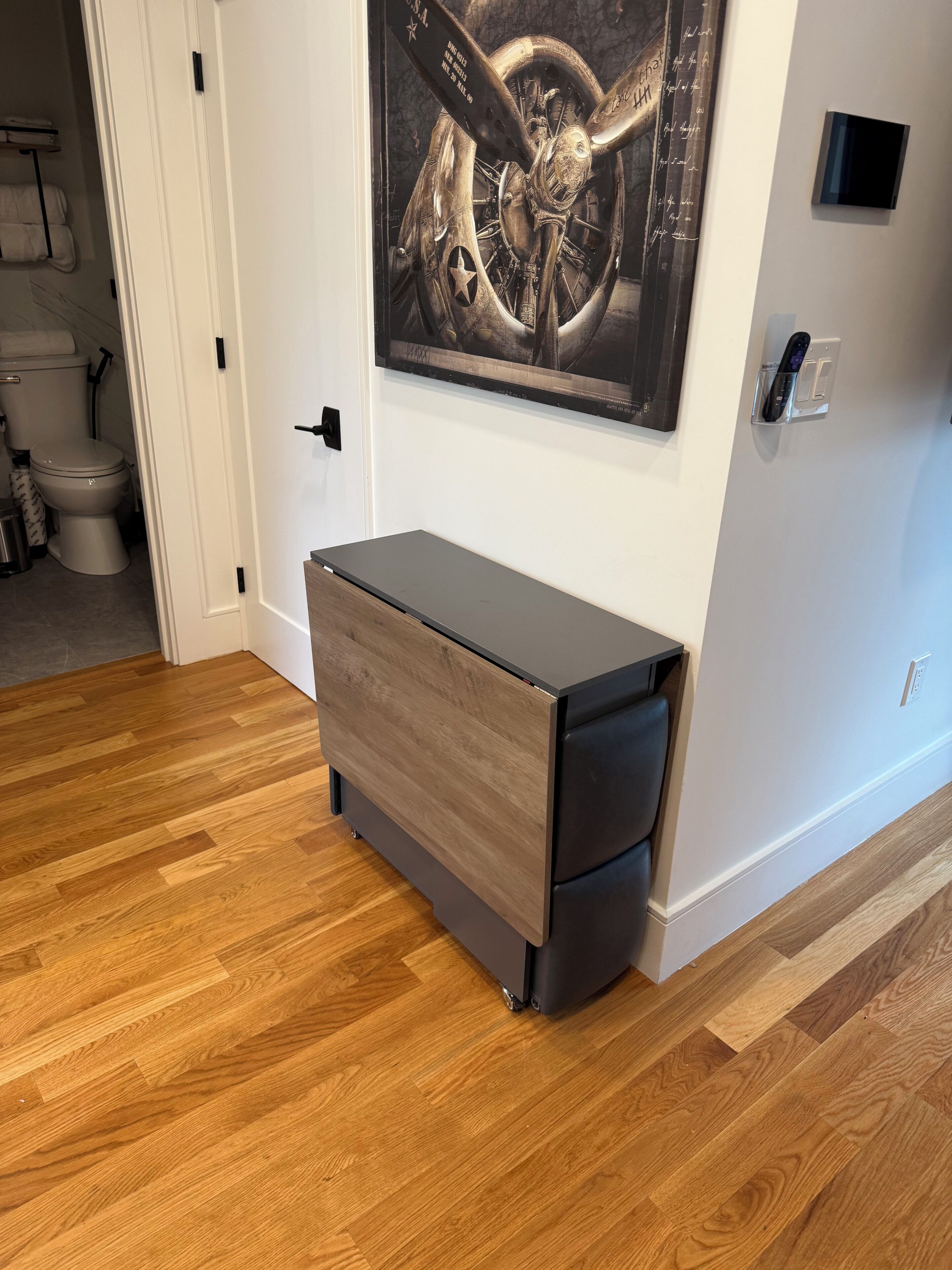 A room with a wooden floor, a grey storage unit, a white door, and a wall-mounted artwork.