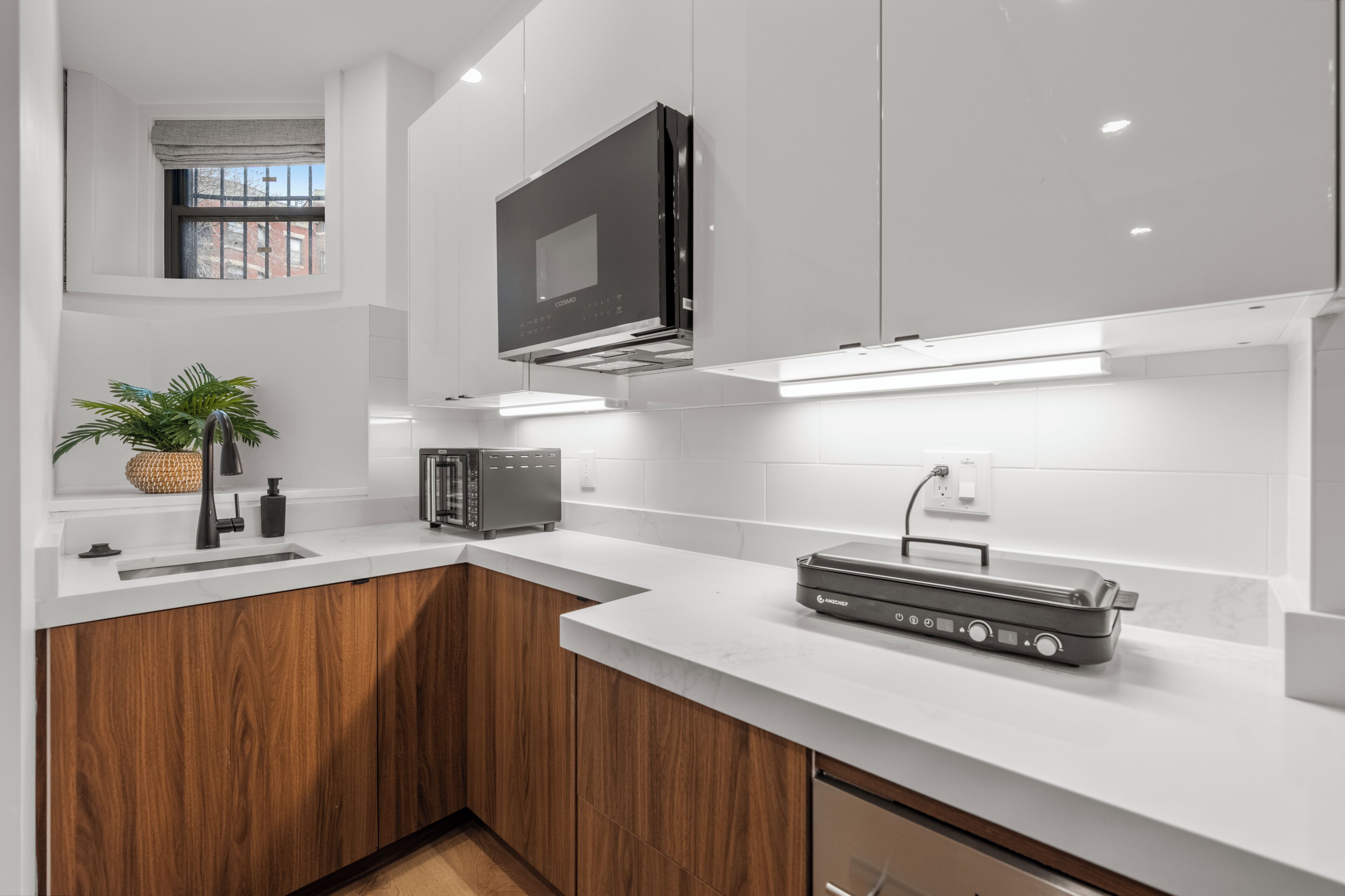 A modern kitchen with white cabinetry, a built-in oven, a microwave, and a portable grill.