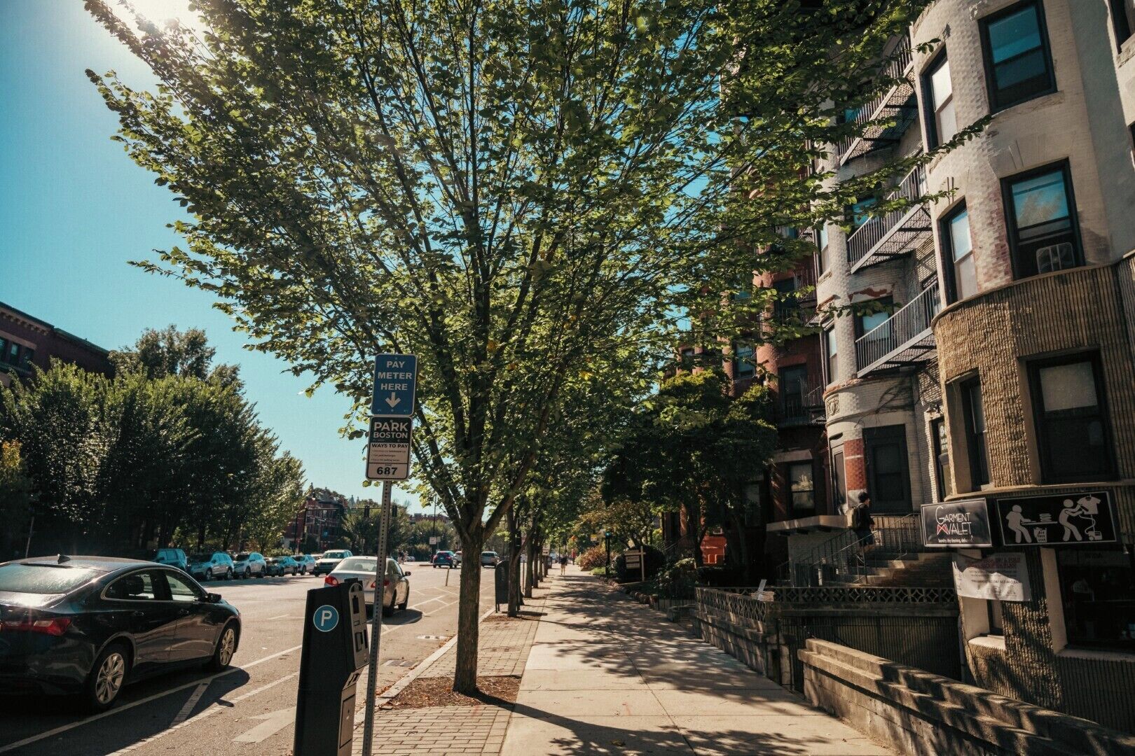 A street lined with trees and parked cars, with a building featuring a sign for Garment Atelier.