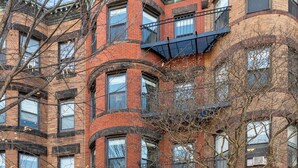 Un edificio de ladrillo de varios pisos, con una entrada central, ventanas amplias y una escalera de incendios.