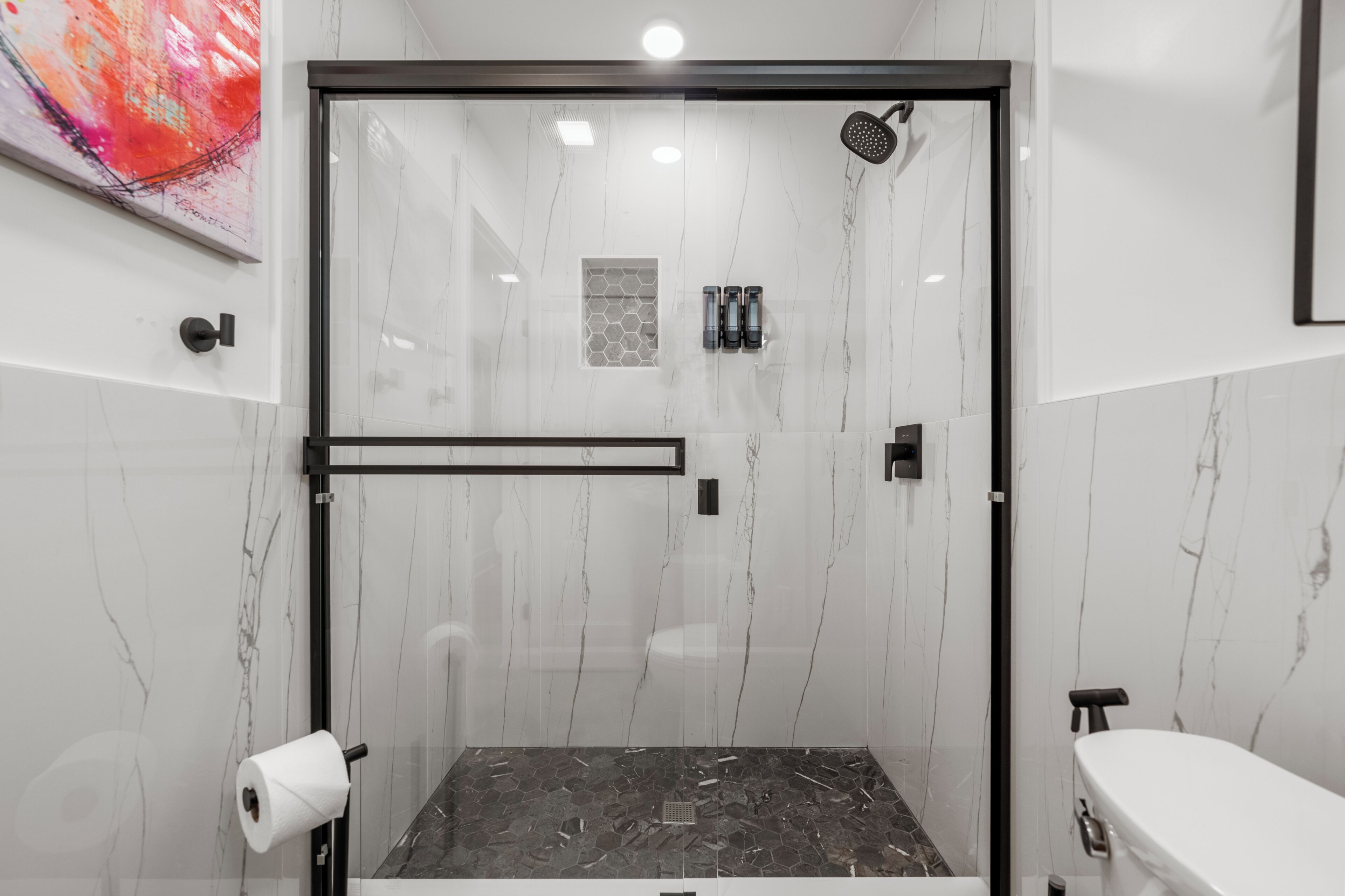 A modern bathroom with a glass-enclosed shower, a toilet, and a sink.