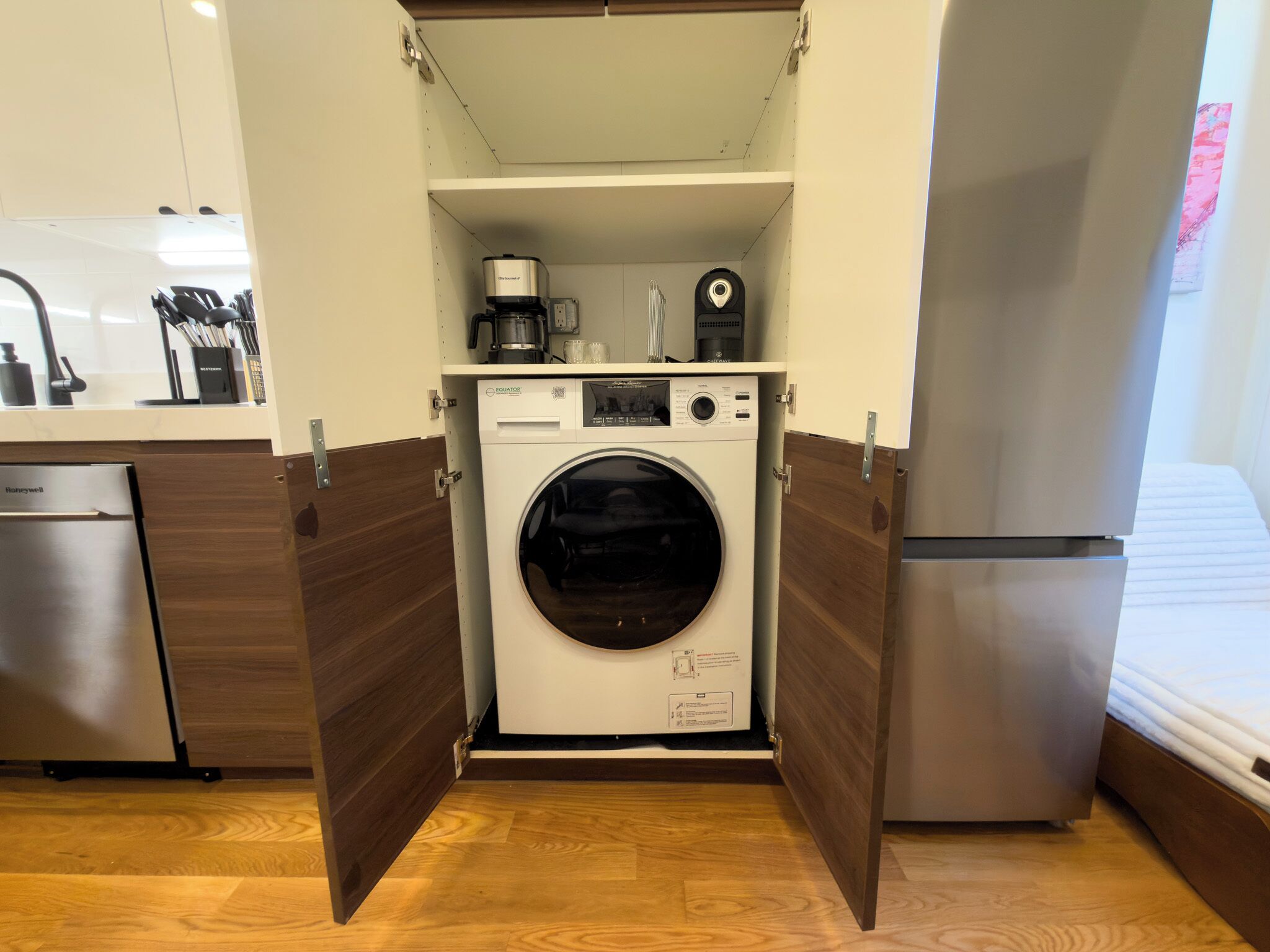 A compact laundry room with a front-loading washing machine, a coffee maker, and a small shelf with kitchen utensils.