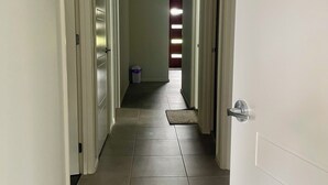 Käytävä, jossa on valkoiset ovet, laattalattia ja kauempana roskakori.