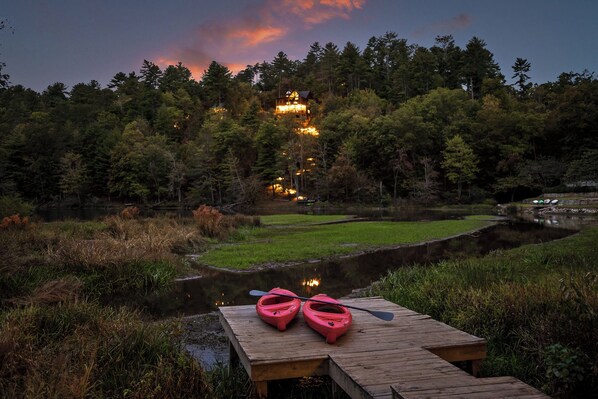 A wooden dock with kayaks and a forested area with a building in the background. - The Hidden Still~Blue Ridge Speakeasy Lakehouse~SLEEPS 22 (Cherry Log)