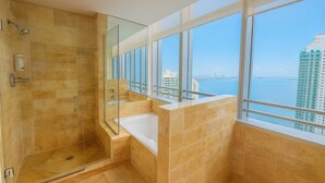 A modern bathroom with a glass-enclosed shower, a bathtub, and large windows offering a city view.