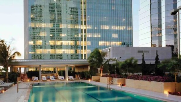 A modern hotel with a swimming pool, lounge chairs, and a view of high-rise buildings.