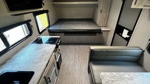 A compact RV interior with a kitchenette, a bed, and a seating area. - Private campground with camper rental in charming Ridgeway (Ridgeway)