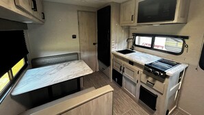 A compact RV kitchen with a stove, sink, and a small dining area. - Private campground with camper rental in charming Ridgeway (Ridgeway)
