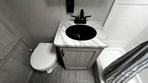 A compact bathroom with a white toilet, a sink with a black faucet, and a marble countertop. - Private campground with camper rental in charming Ridgeway (Ridgeway)