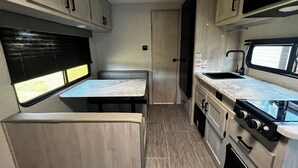 A compact RV kitchen with a dining area, a stove, and a sink. - Private campground with camper rental in charming Ridgeway (Ridgeway)