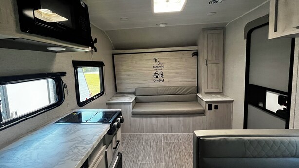 A compact RV interior with a kitchenette, a seating area, and a wall decal. - Private campground with camper rental in charming Ridgeway (Ridgeway)