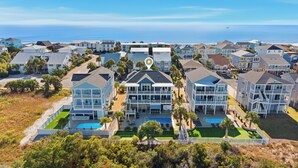 A beachfront property with multiple two-story buildings, a swimming pool, and a view of the ocean. - Luxurious, Newly Furnished Home w/ stunning views & just steps from the beach (Ocean Isle Beach)