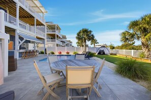 A poolside area with a wooden table and chairs, a small pool, and a two-story building with balconies. - Luxurious, Newly Furnished Home w/ stunning views & just steps from the beach (Ocean Isle Beach)