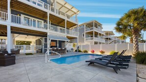 A pool area with lounge chairs, a small pool, and a building with multiple balconies. - Luxurious, Newly Furnished Home w/ stunning views & just steps from the beach (Ocean Isle Beach)