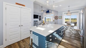 A modern kitchen with a large island, a dining area with a view, and a pantry sign on the door. - Luxurious, Newly Furnished Home w/ stunning views & just steps from the beach (Ocean Isle Beach)