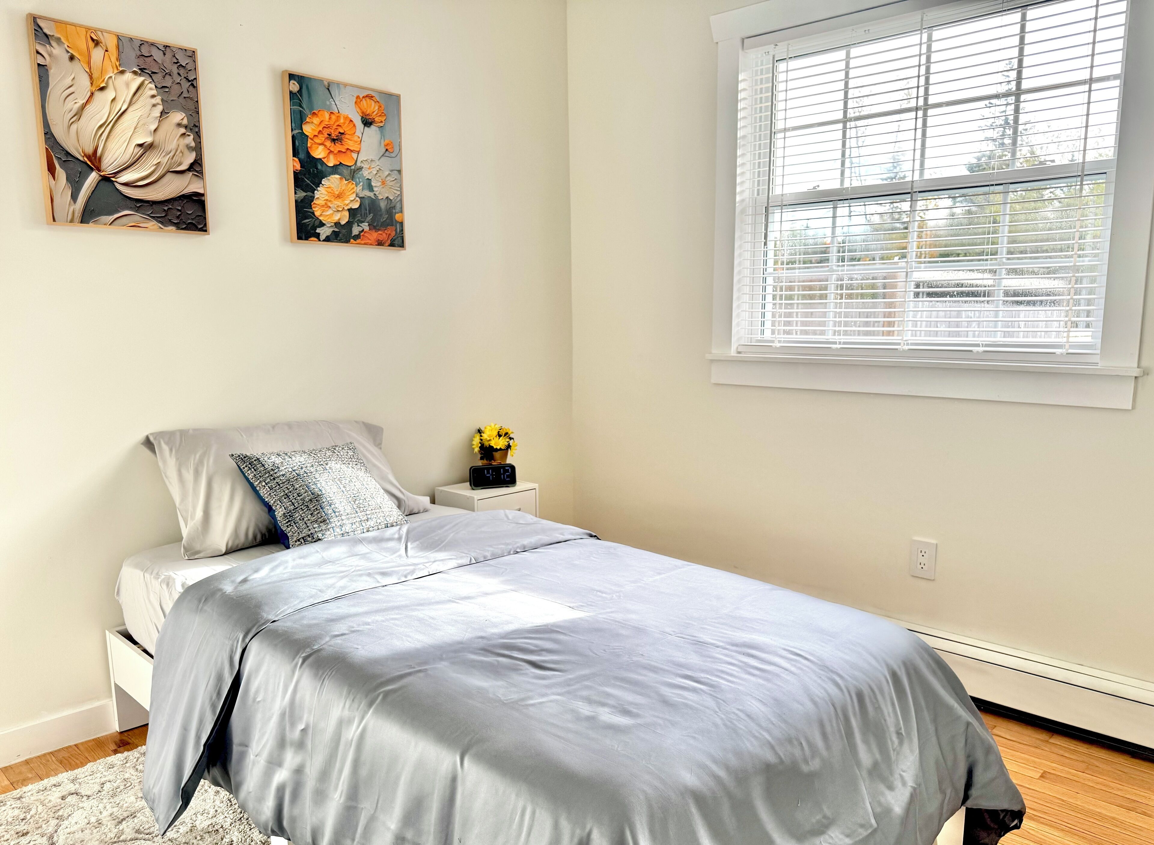 A bedroom with a bed, a nightstand with a clock, and two wall-mounted paintings.