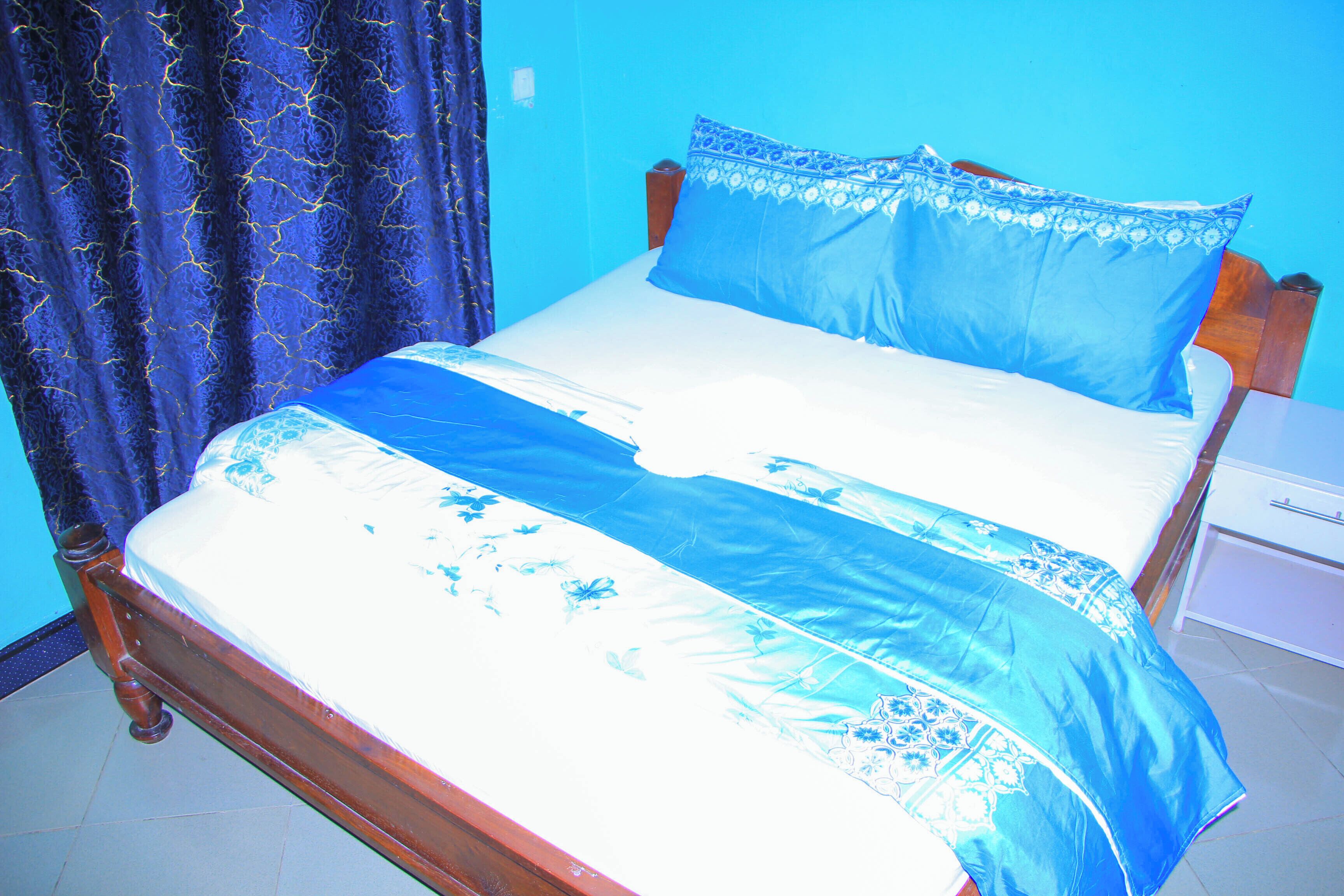 A bed with a blue and white bedspread, a wooden headboard, and a nightstand with a drawer.