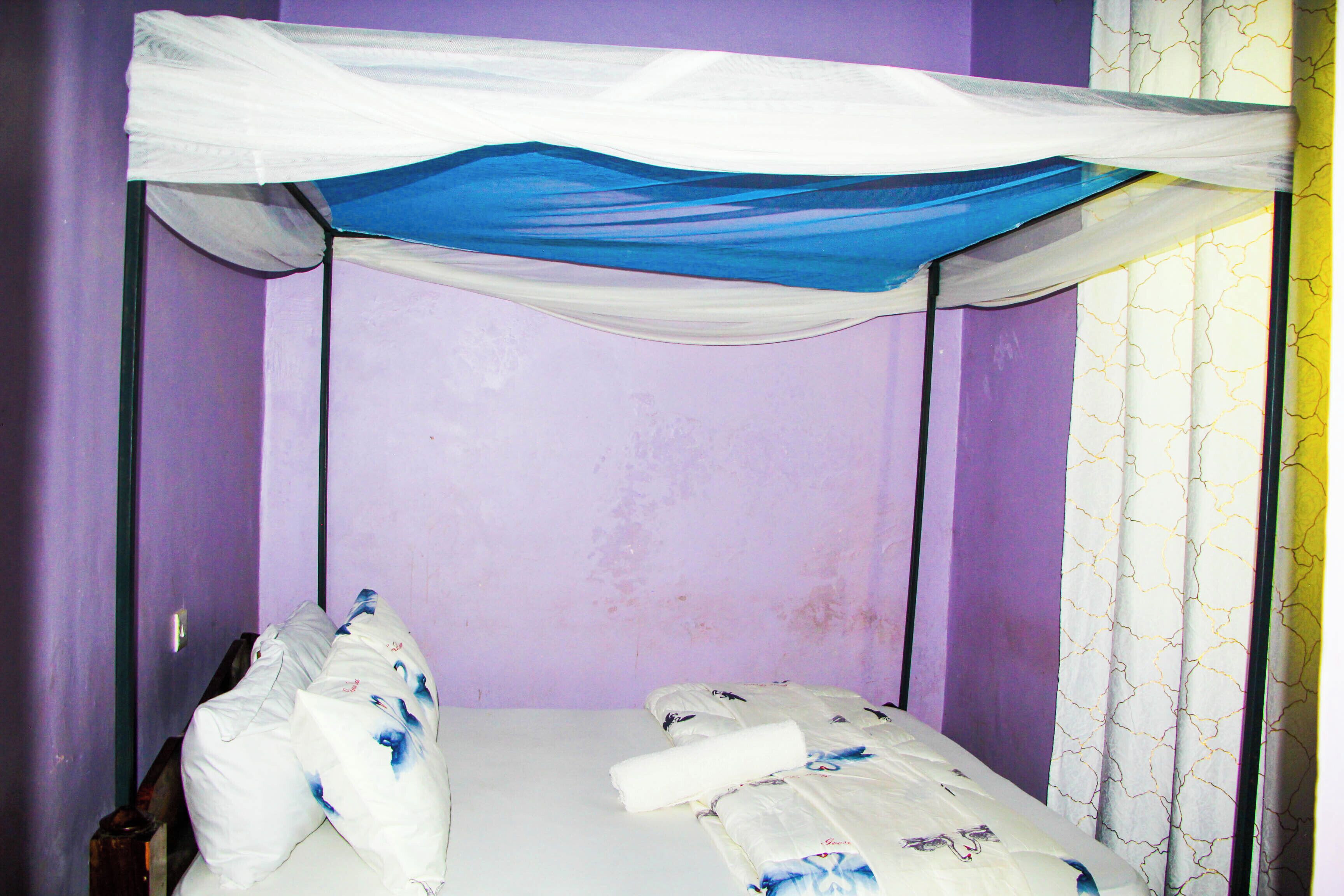 Una cama individual con dosel, una pared lisa y una ventana con cortinas estampadas.