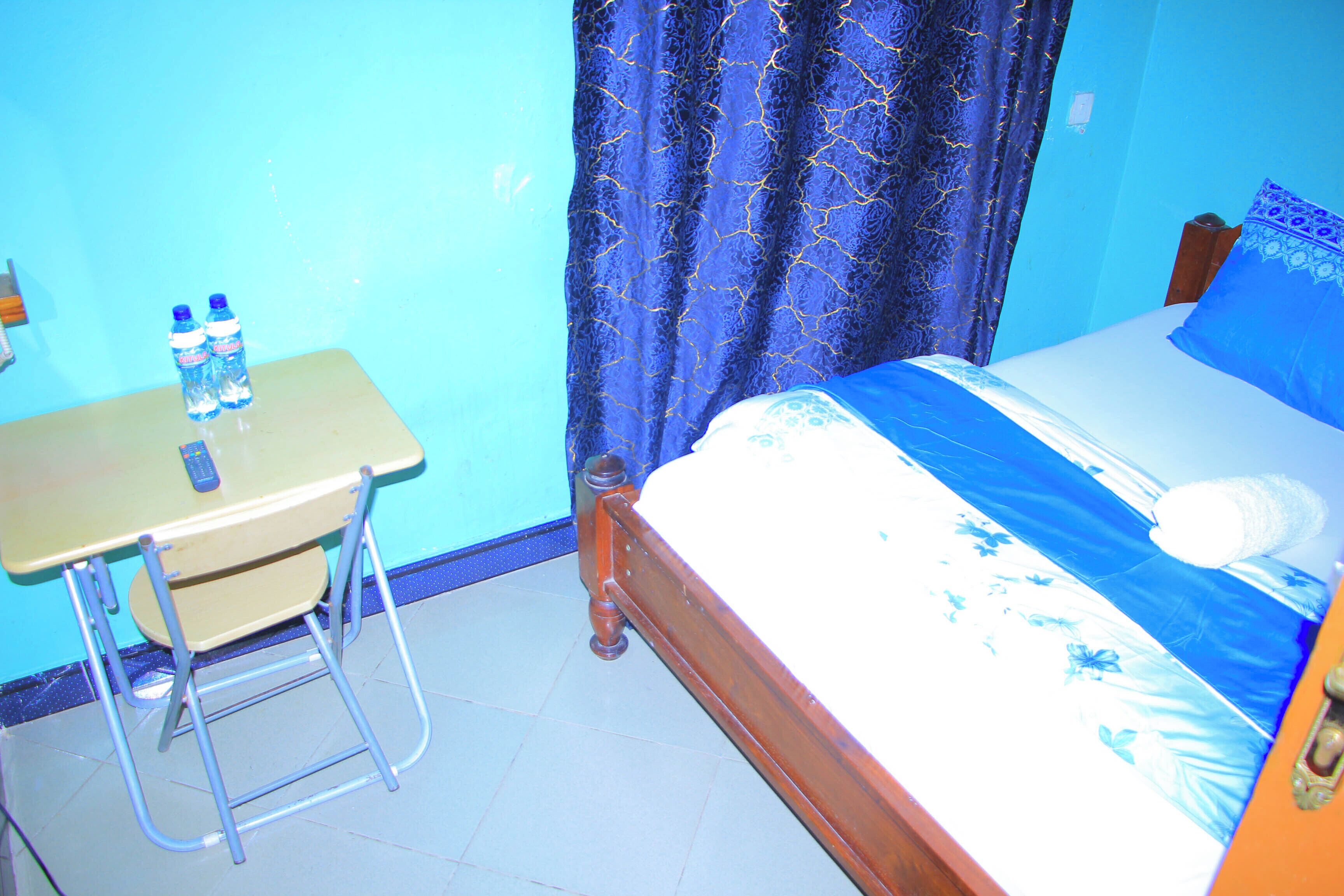 A bedroom with a bed, a desk, and two water bottles.