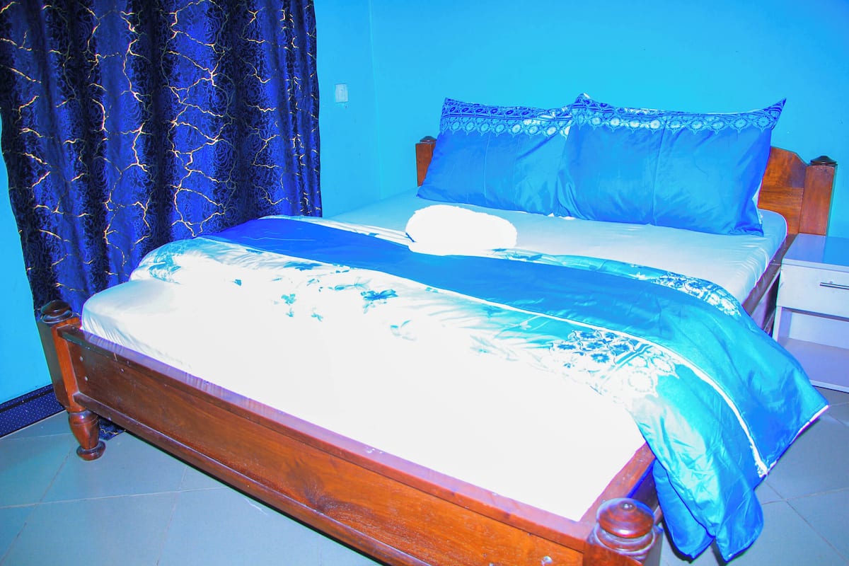 Uma cama com estrutura de madeira, colcha azul e almofadas combinando.