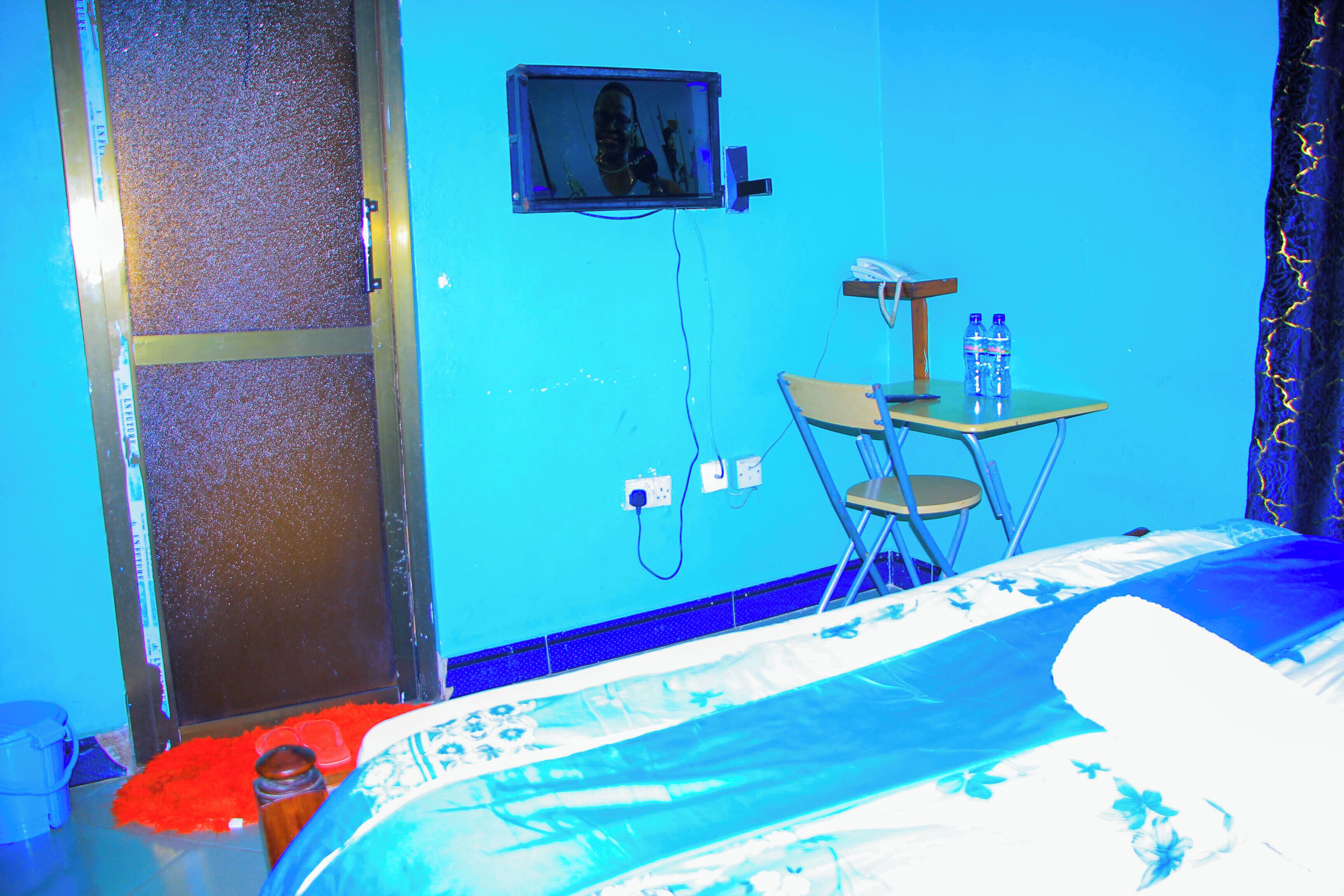 A room with a bed, a desk with a chair, a television mounted on the wall, and a water bottle on the desk.